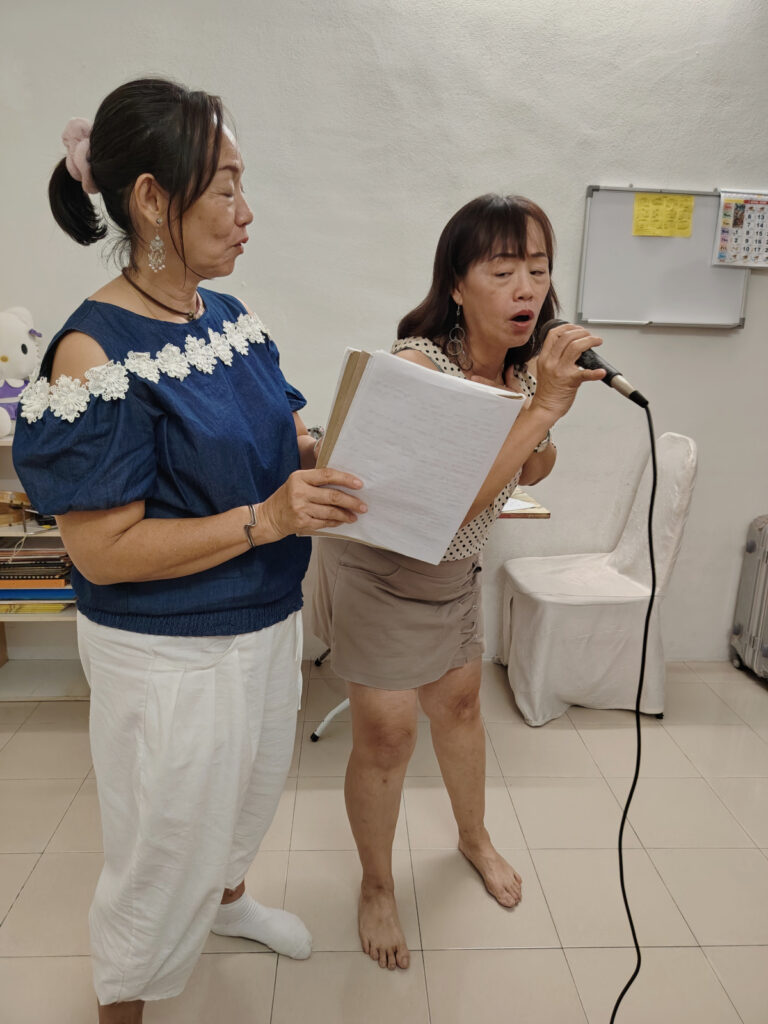 Two adult student one is singing while the other holds a music score during class