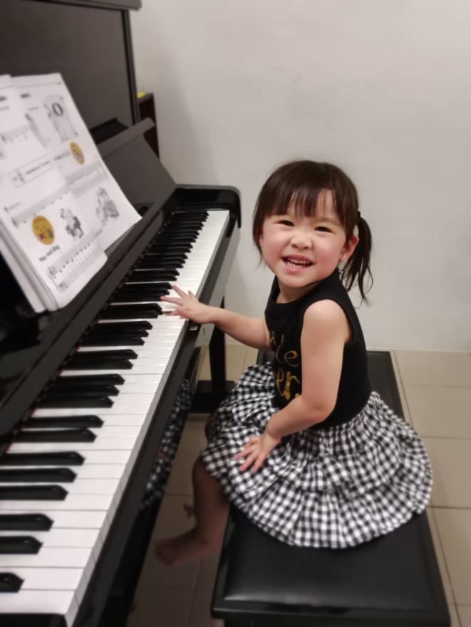 Child playing piano and smiling at the camera during piano class