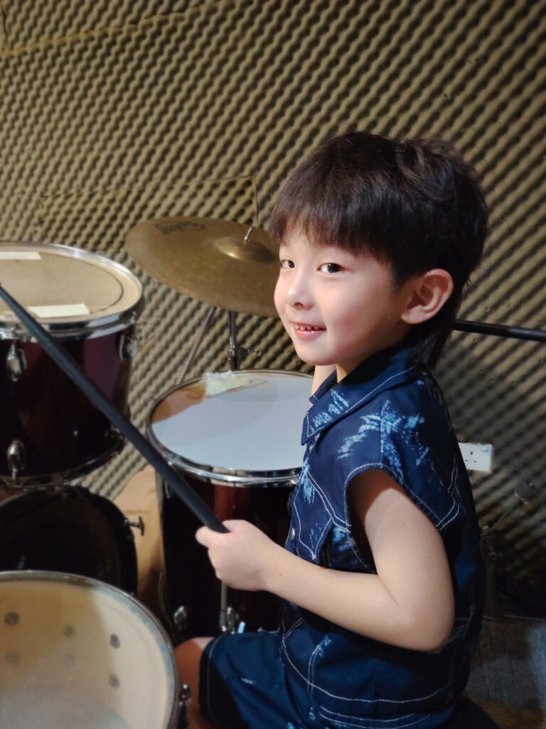 Child playing drums in lesson while looking toward instructor off-frame