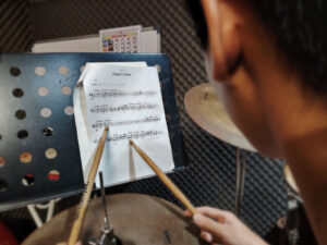 Person using a drumstick to point at sheet music while reading
