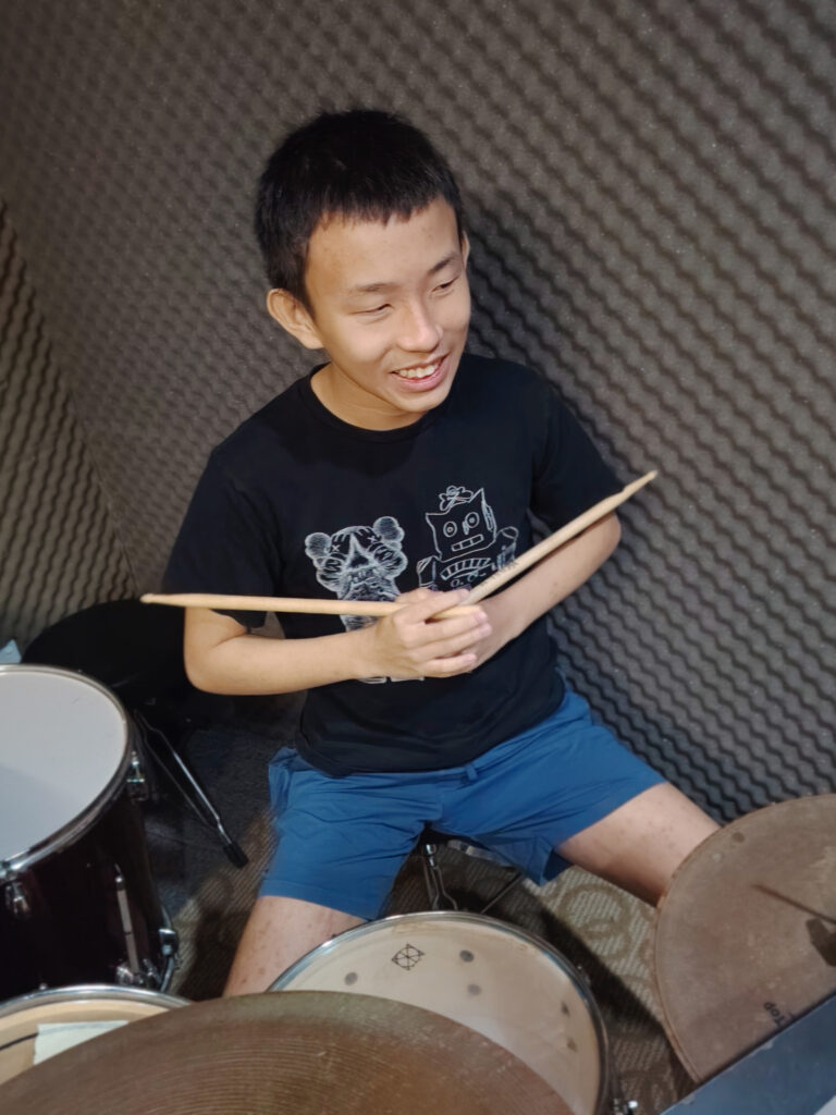 Young student holding a drumstick in an unusual way while smiling toward teacher off-camera